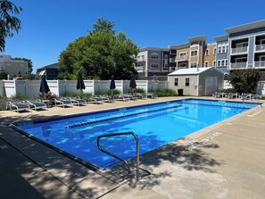 A swimming pool with lounge chairs and umbrellas, surrounded by multi-story buildings. - Rooftop Sunsets, EV Charger, Pool & Steps to Beach (New Buffalo)