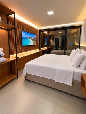 Ein modernes Hotelzimmer mit einem großen Bett, einem an einer Holzvertäfelung montierten Fernseher und Blick auf den Strand durch eine Glastür.