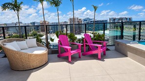 Eine Dachterrasse mit Korbmöbeln und leuchtend rosa Stühlen mit Blick auf eine Stadtlandschaft.
