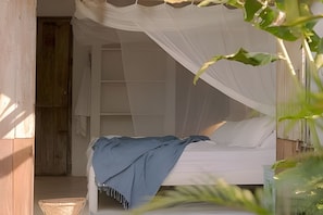 Una habitación con una cama bajo un dosel blanco, una puerta de madera y una planta en primer plano.