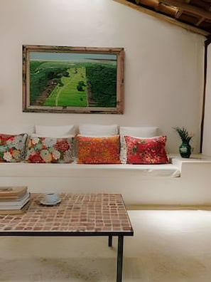 Ein Zimmer mit einer Sofagarnitur, die an einer Wand platziert ist, einem gerahmten Gemälde darüber und einem Tisch mit Rautenmuster davor.