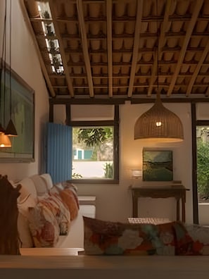 Una habitación con techo de madera, una cama con almohada de colores, un cuadro en la pared y una ventana con vistas al verde.