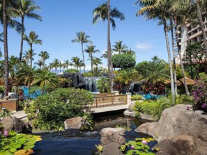 Un complexe hôtelier tropical doté d’une cascade, de palmiers, d’un pont et d’un espace piscine.