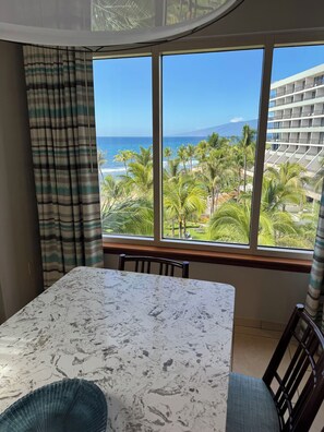 A room with a large window offering a view of a beach and palm trees. - Kaanapali Beach Maui  3-bedroom condo, ocean front walk out Lanai. 4 large pools (Lahaina)