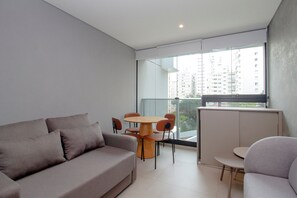 A modern living room with a sofa, a dining table with chairs, and a view of high-rise buildings through large windows. - Duo Corporate Lifestyle by Housi (São Paulo)
