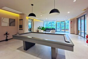 A pool table in a modern room with large windows, a sofa, and a potted plant. - Duo Corporate Lifestyle by Housi (São Paulo)