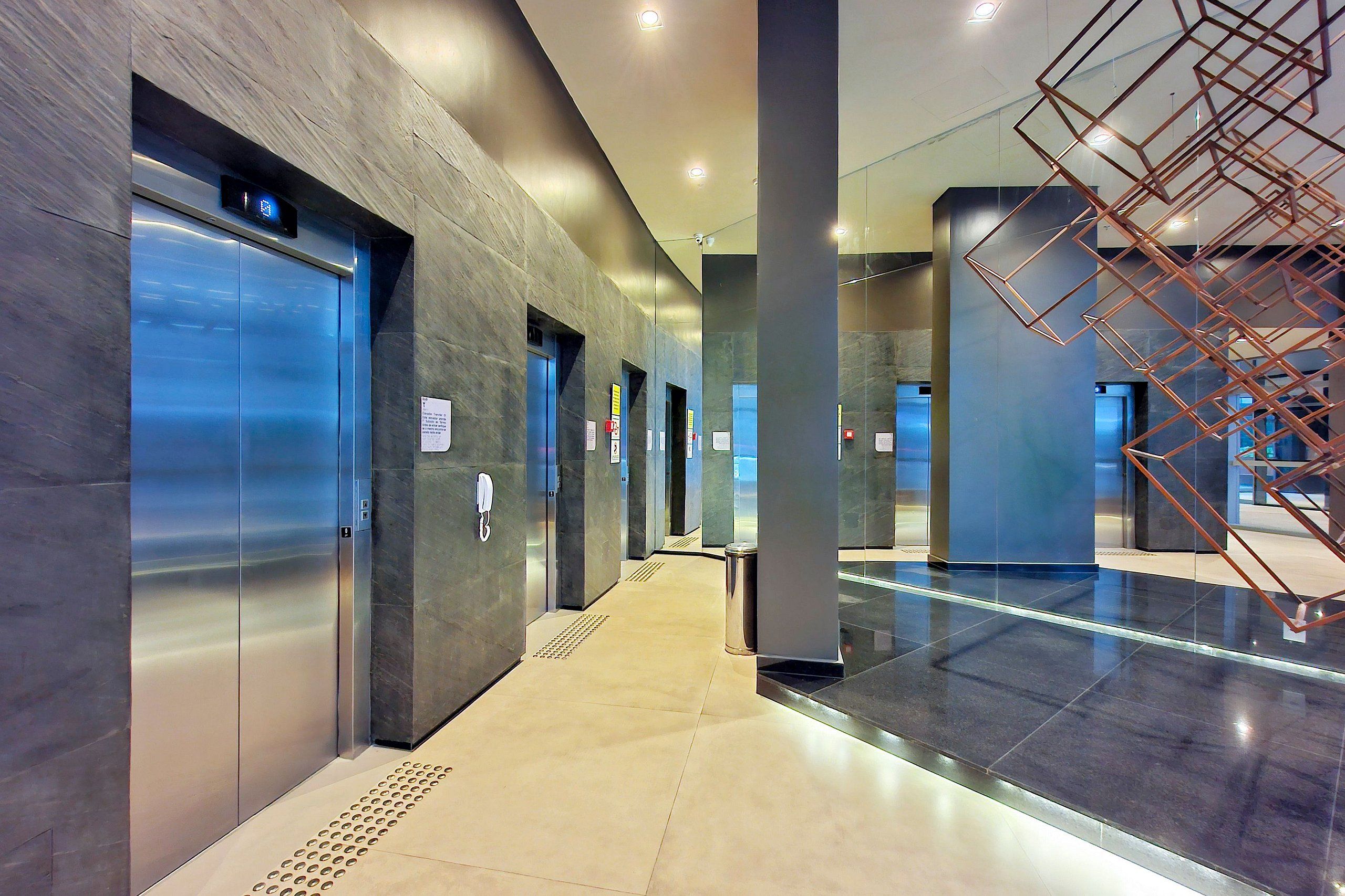 A modern elevator area with metallic elevators, a patterned wall, and a geometric metal structure.