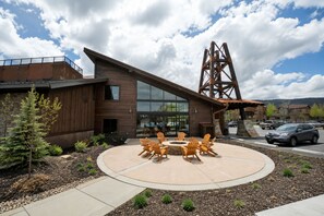Edifici modern amb façana de fusta, grans finestres i una zona d'estar exterior circular amb cadiretes Adirondack.