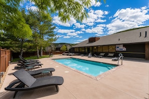 An outdoor swimming pool with lounge chairs, a covered seating area, and a building with a sign. - Romantic Retreat - 4 Min to Skiing (Park City)