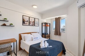 Una habitación de hotel con cama, escritorio, silla, armario y ventana con cortinas.