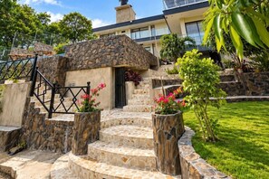 Una escalera de piedra lleva a la entrada de un edificio, rodeada de plantas en macetas y un césped cuidado.