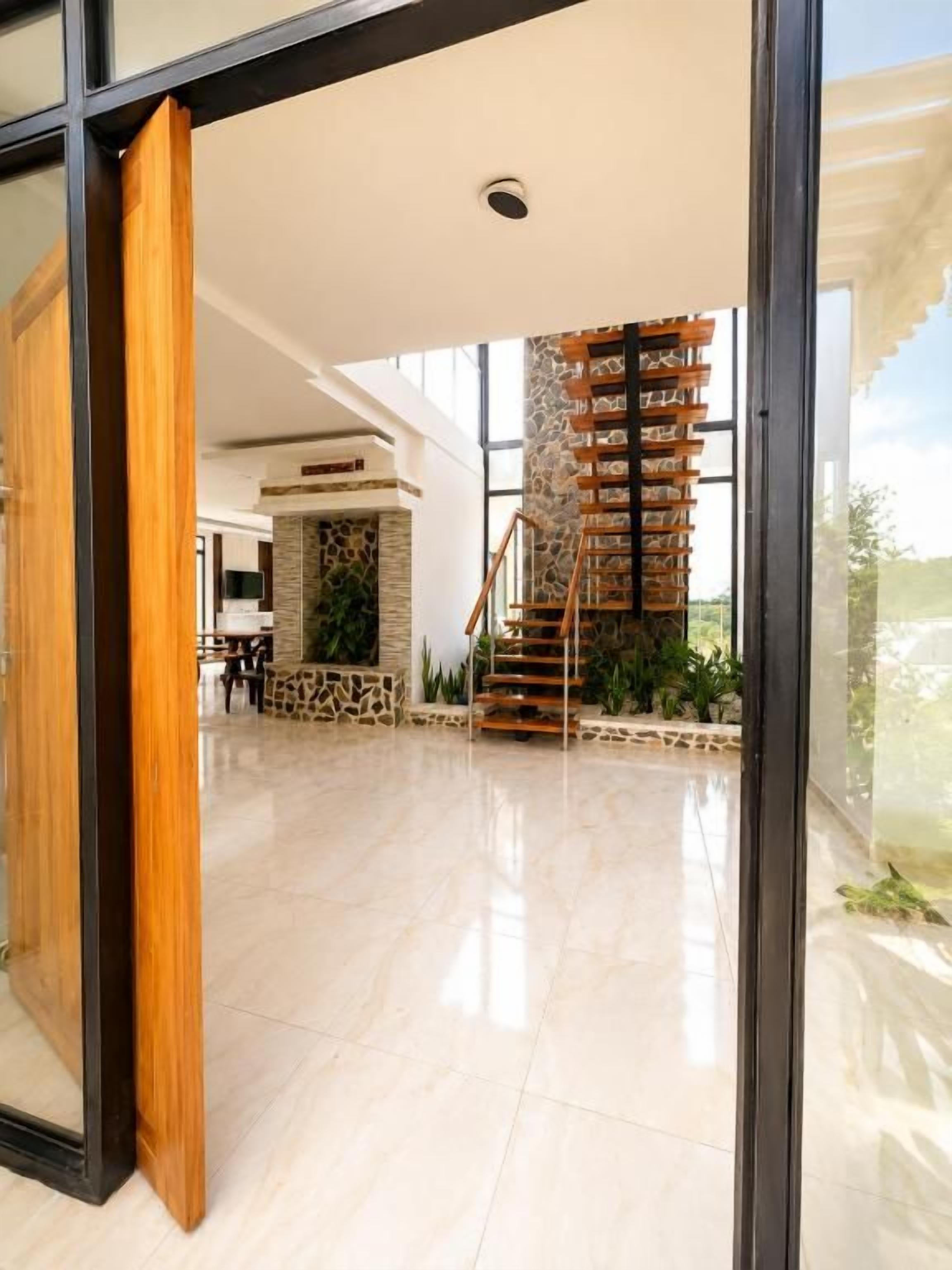 A modern interior with a staircase leading to a balcony, a stone wall, and a glass door.