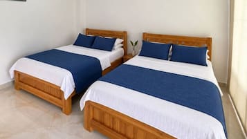 Dos camas de madera con ropa de cama blanca y azul, una planta pequeña en la mesita de noche y un cuadro en la pared.