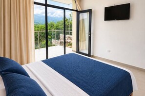 Un dormitorio con cama, televisor montado en la pared y balcón con vistas a zonas verdes.