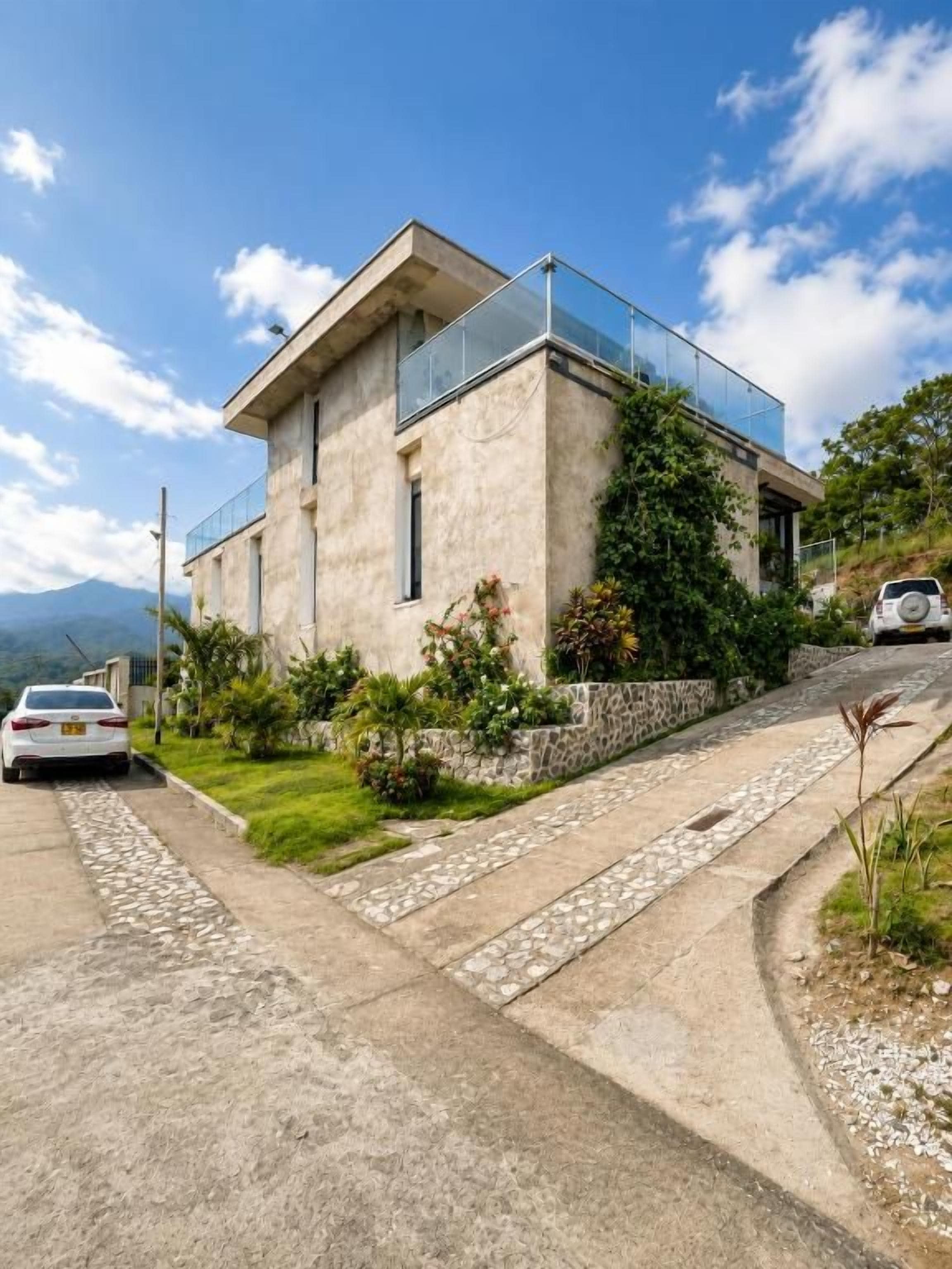 Una casa moderna a due piani con un'auto nel vialetto, immersa nel verde e sotto un cielo sereno.