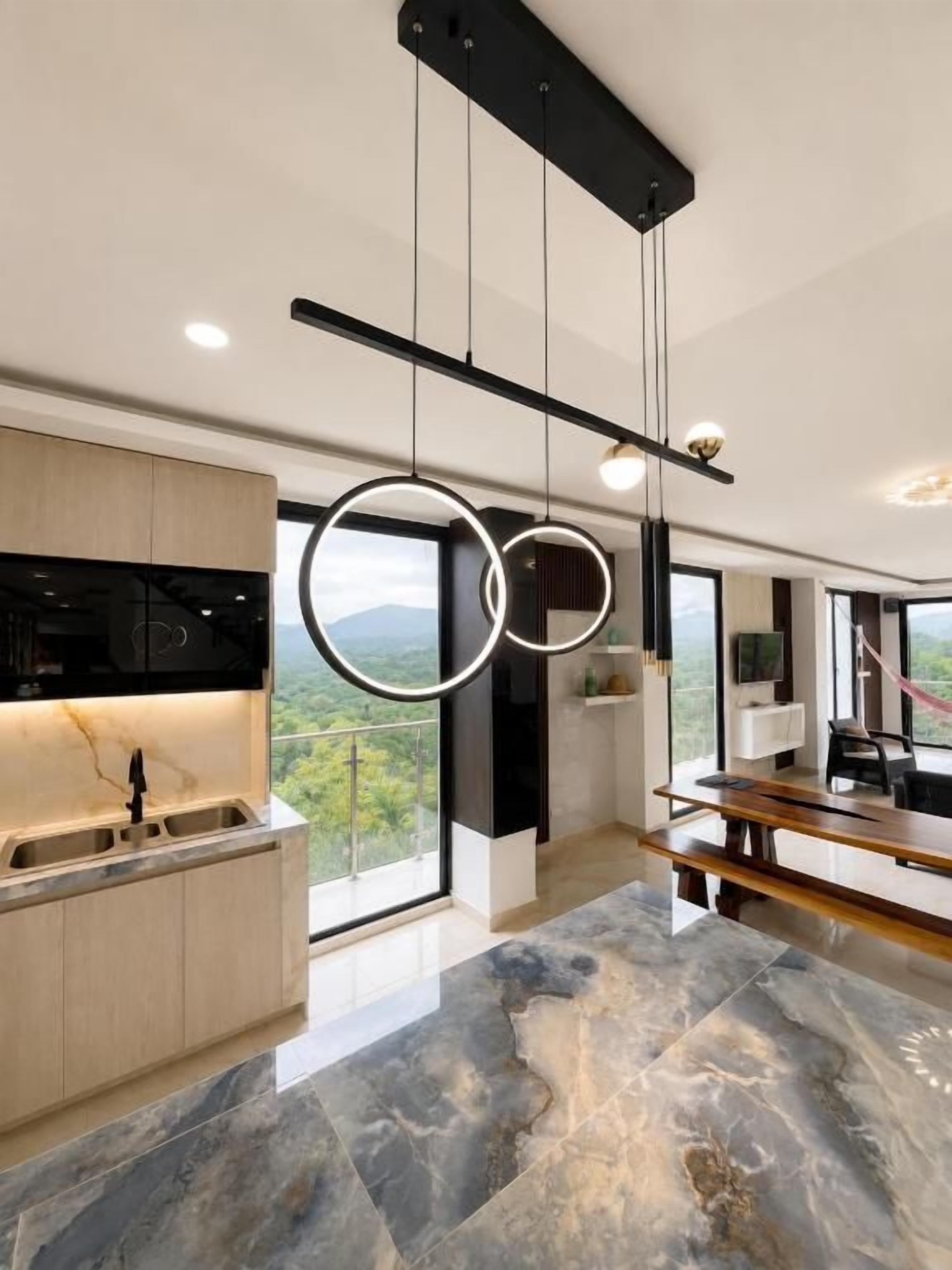 A modern kitchen with a marble floor, pendant lighting, and a view through large windows.