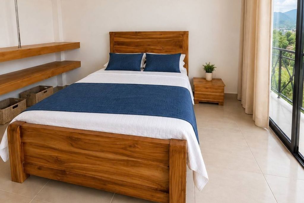 Un dormitorio con una cama de madera, una mesita de noche, una planta en maceta y vistas al verdor a través de una ventana.
