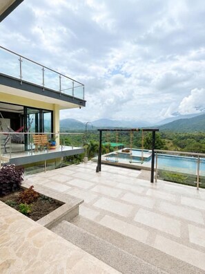 A modern outdoor terrace with a pool, a glass balustrade, and a view of distant mountains. - CABAÑA SANDY HOUSE BY MJS (Santa Marta)