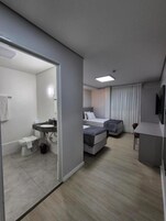 Quarto de hotel moderno com banheiro, cama, escrivaninha e televisão.