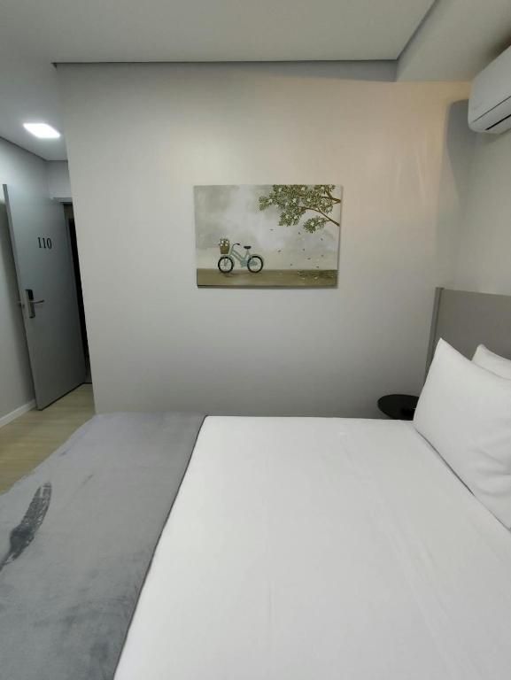 Een hotelkamer met een bed, een schilderij van een fiets aan de muur en een deur met een nummer.