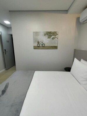 Una habitación de hotel con una cama, una obra de arte colgada en la pared de una bicicleta y una puerta con un número.