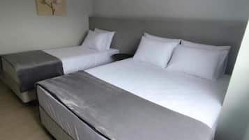 Habitació d'hotel amb dos llits, un sofà gris, un terra de fusta i un aire condicionat fixat a la paret.
