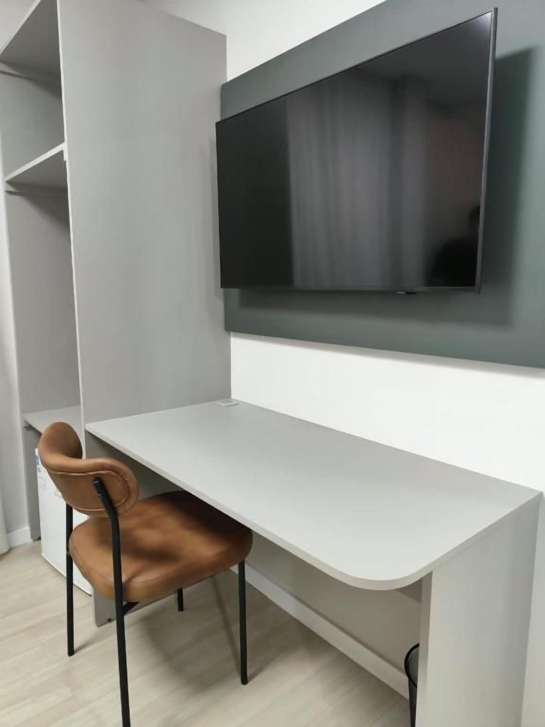 Een moderne kamer met een wit bureau, een bruine stoel en een wandgemonteerde flatscreen-tv.
