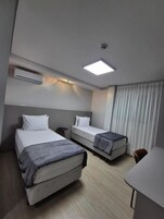 Quarto de hotel com duas camas, uma mesa e uma cadeira.