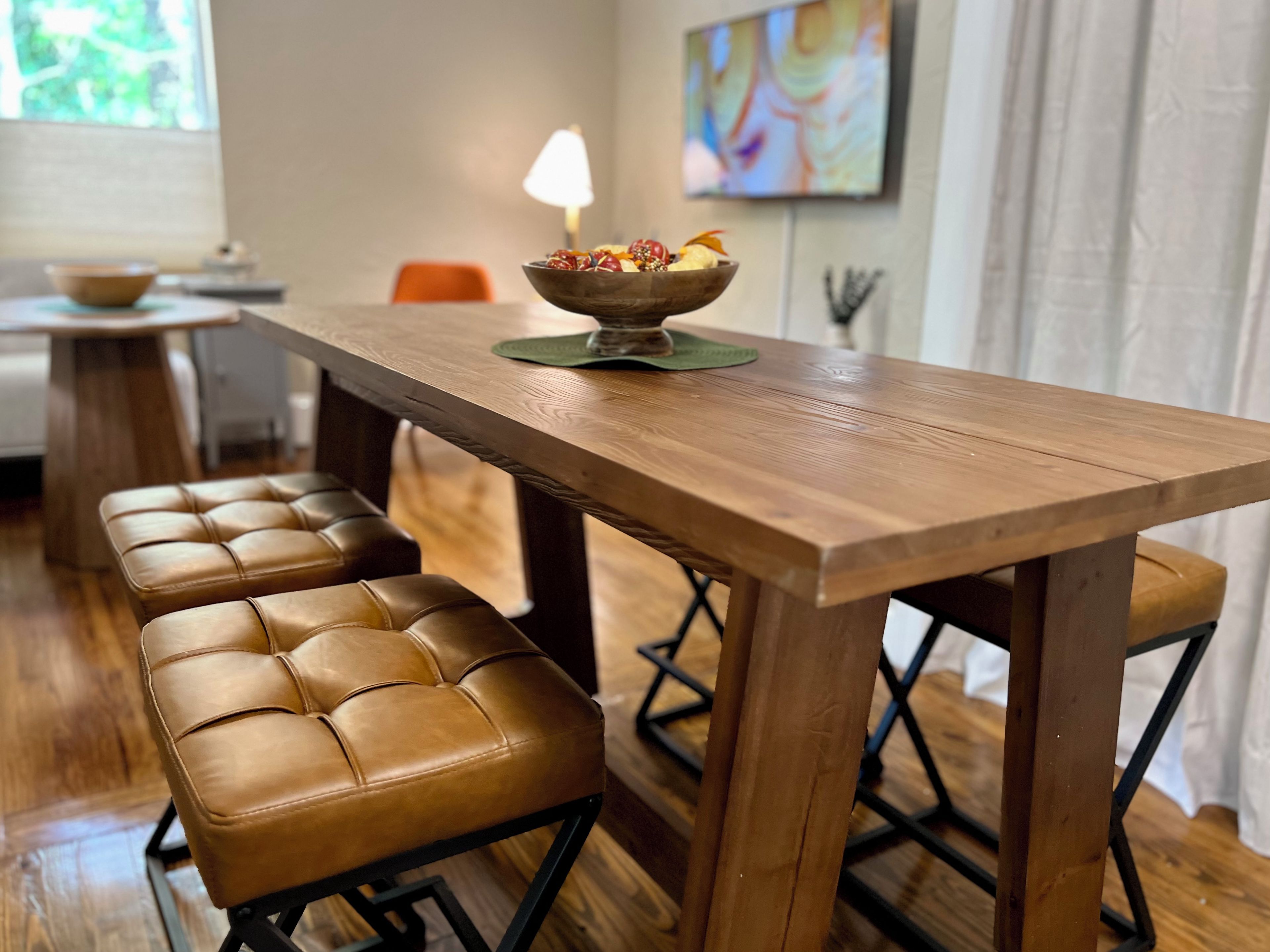 A wooden dining table with a bowl of fruit and a lamp on it.