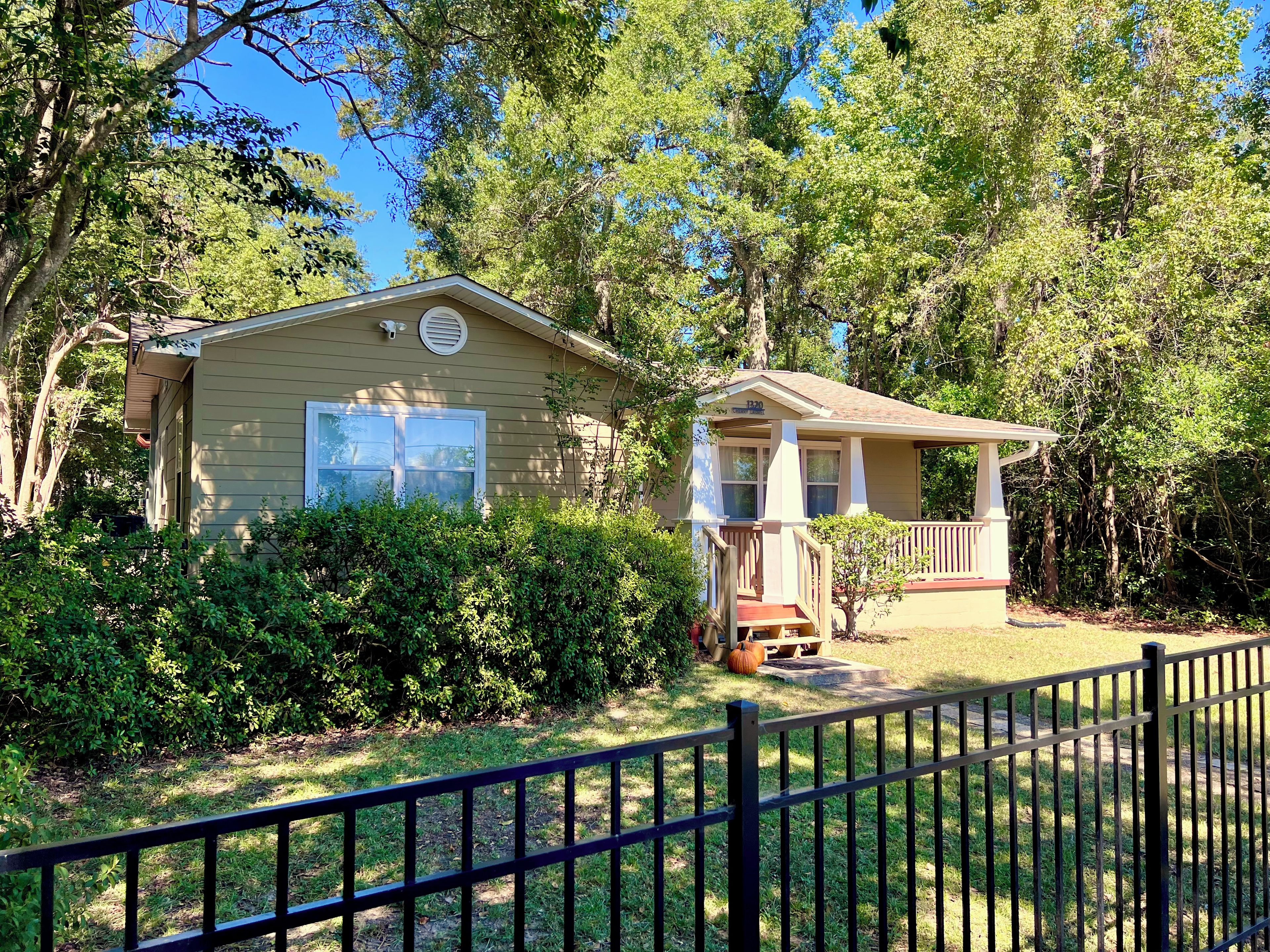A single-story house with a porch, surrounded by dense greenery and trees.