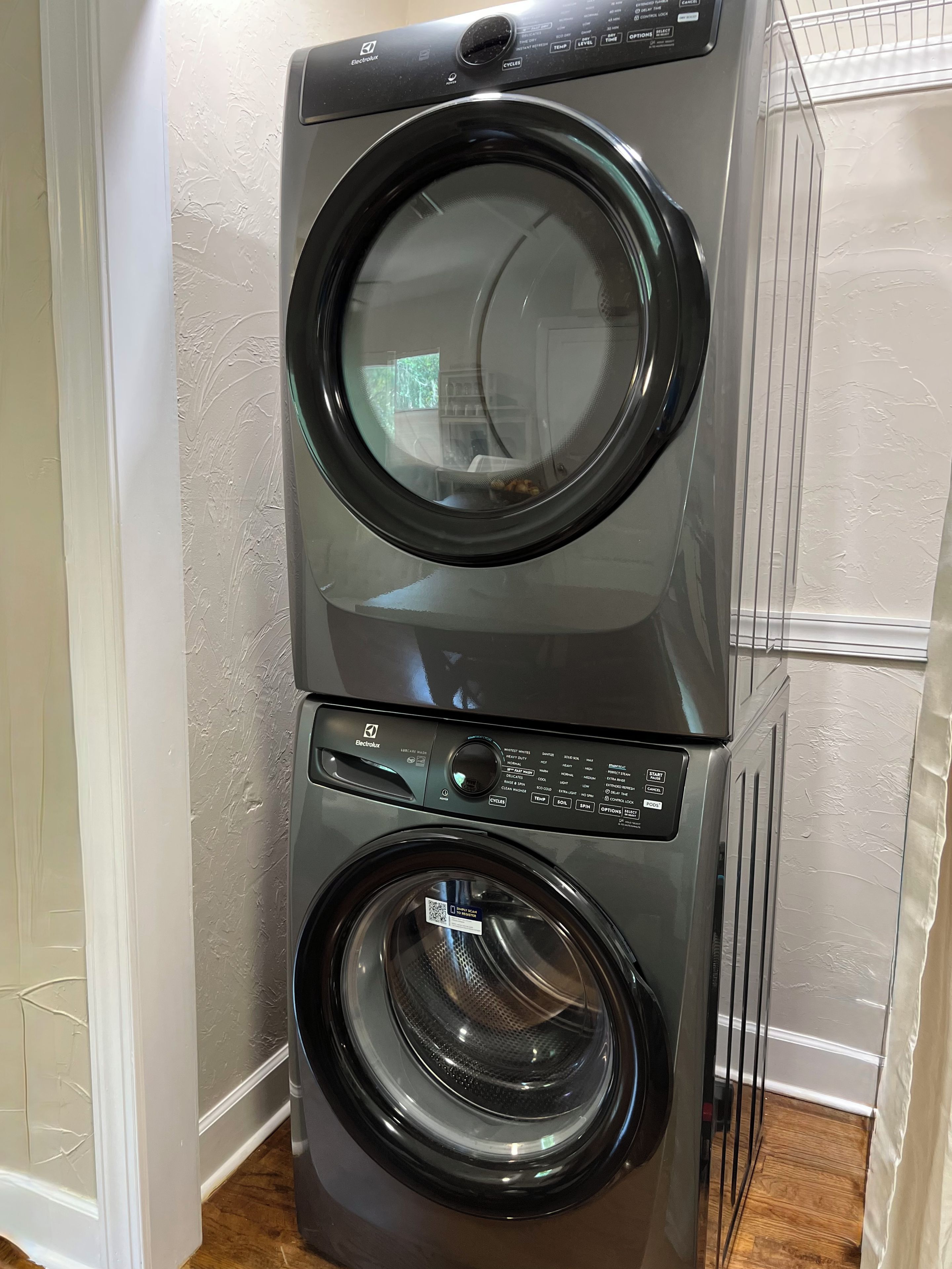A stacked washer and dryer unit with control panel, in a room with textured walls and wooden flooring.