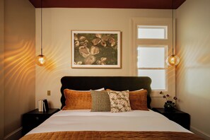 A bedroom with a bed, two bedside tables, a nightstand, a framed artwork, and a window. - 9BR Historic Inn | Pool, Sauna & Outdoor Theater (New Orleans)