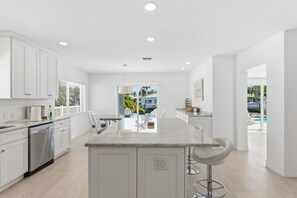 A modern kitchen with white cabinetry, a marble island, and a dining area with a view of the outdoors. - Pompano Waterfront | Heated Pool, 50' Dock, Pets (Pompano Beach)