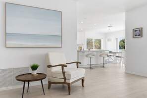 Un soggiorno moderno con un quadro di grandi dimensioni, una poltrona confortevole, un tavolino con una pianta e vista sull'area cucina.