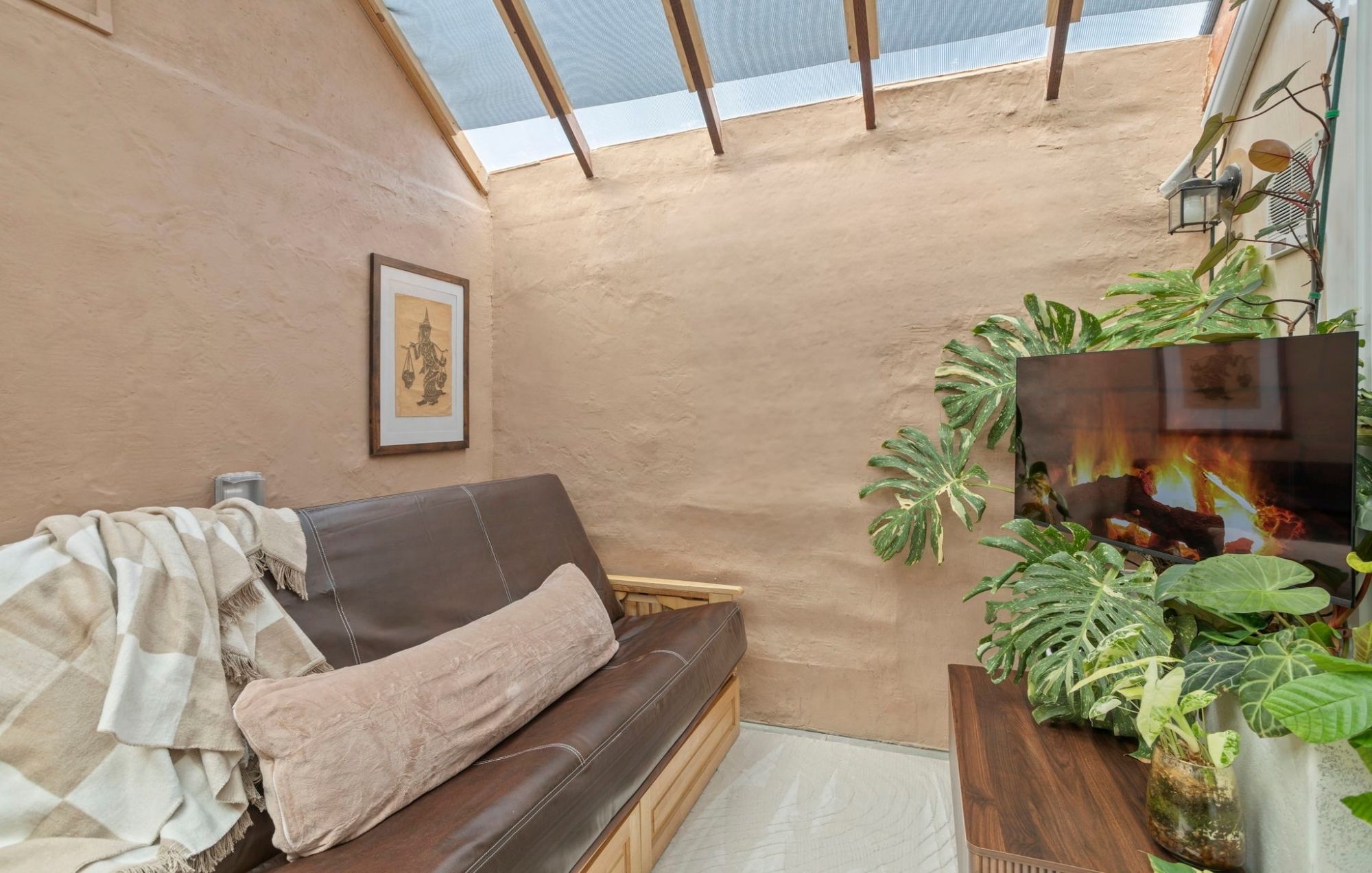 A cozy room with a brown leather sofa, a framed picture on the wall, and a large window with a view of the sky.