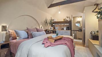 Un dormitorio moderno con una cama grande, mesitas de noche, una lámpara de noche, una planta en maceta y vistas a la cocina contigua.