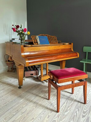 A grand piano with a bench and a stool, accompanied by a vase of flowers and a book on the piano. - Renovated old school from 1927 close to the sea (Ulfborg)