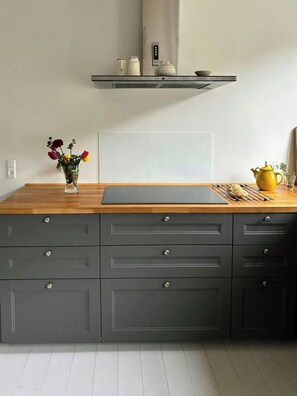 A kitchen with a wooden countertop, grey cabinets, a vase with flowers, and a yellow teapot. - Renovated old school from 1927 close to the sea (Ulfborg)