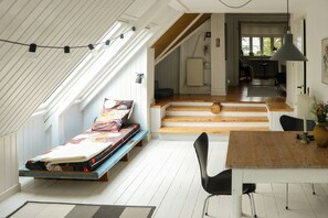 Dormitorio estilo loft con cama, mesa de comedor y una silla. Una escalera conduce a un nivel superior.