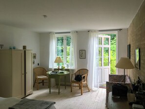 Een kamer met een bed, een tafel met stoelen, een radiator en een raam met gordijnen.