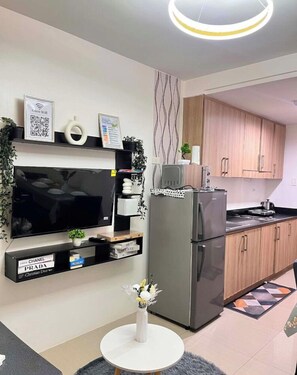 A modern kitchen with a built-in TV, a refrigerator, wooden cabinets, and a small dining table. - STAYCATION SUITES PH 2 (Pasay City)