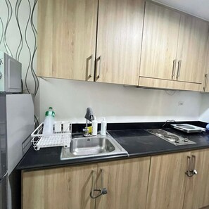 A kitchen with wooden cabinets, a stainless steel sink, and a countertop with various items. - STAYCATION SUITES PH 2 (Pasay City)