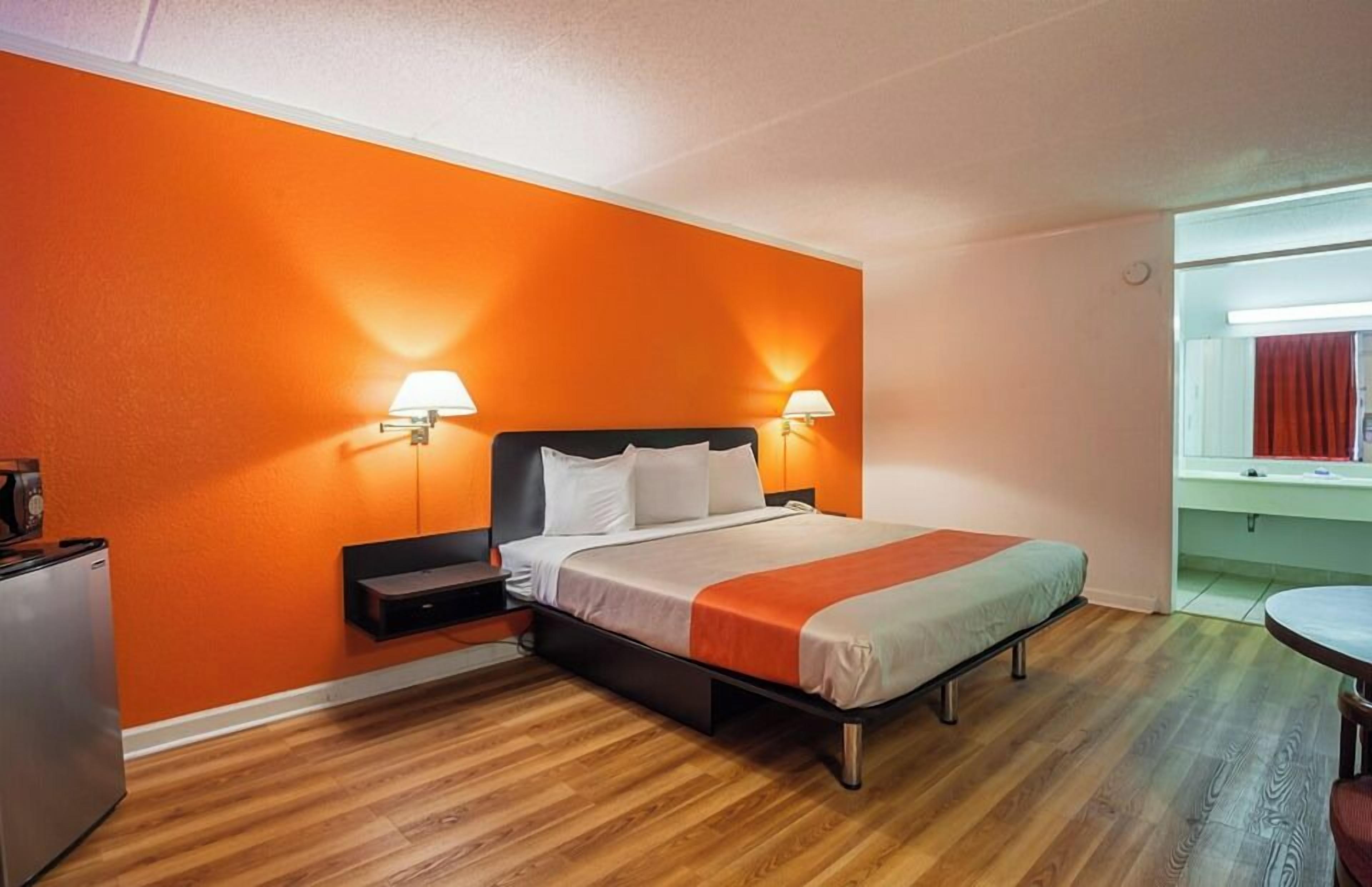 Una habitación de hotel con cama, lámparas de noche, una mesita y una ventana con cortinas.