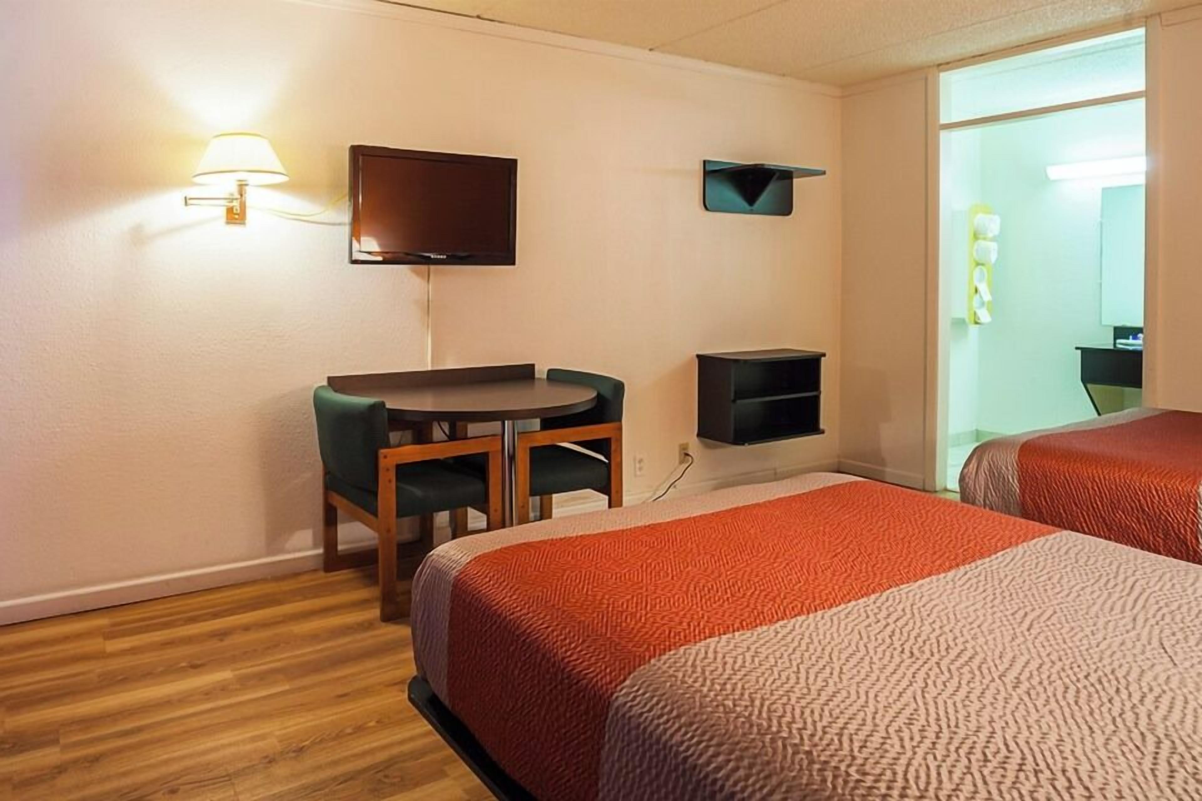 Une chambre d’hôtel avec deux lits, un bureau, une chaise, une télévision et une salle de bain visible à travers une porte ouverte.