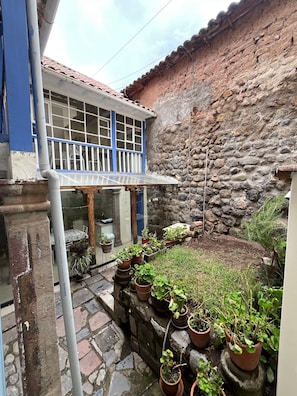 Un patio con muro de piedra, plantas en macetas y un edificio con puerta y ventanas azules.