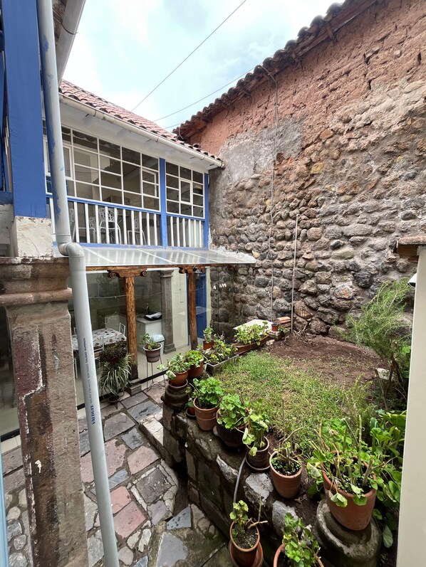 A courtyard with a stone wall, potted plants, and a building with a blue door and windows. - Casa Waynapata Centro Histórico Cusco (Cusco)