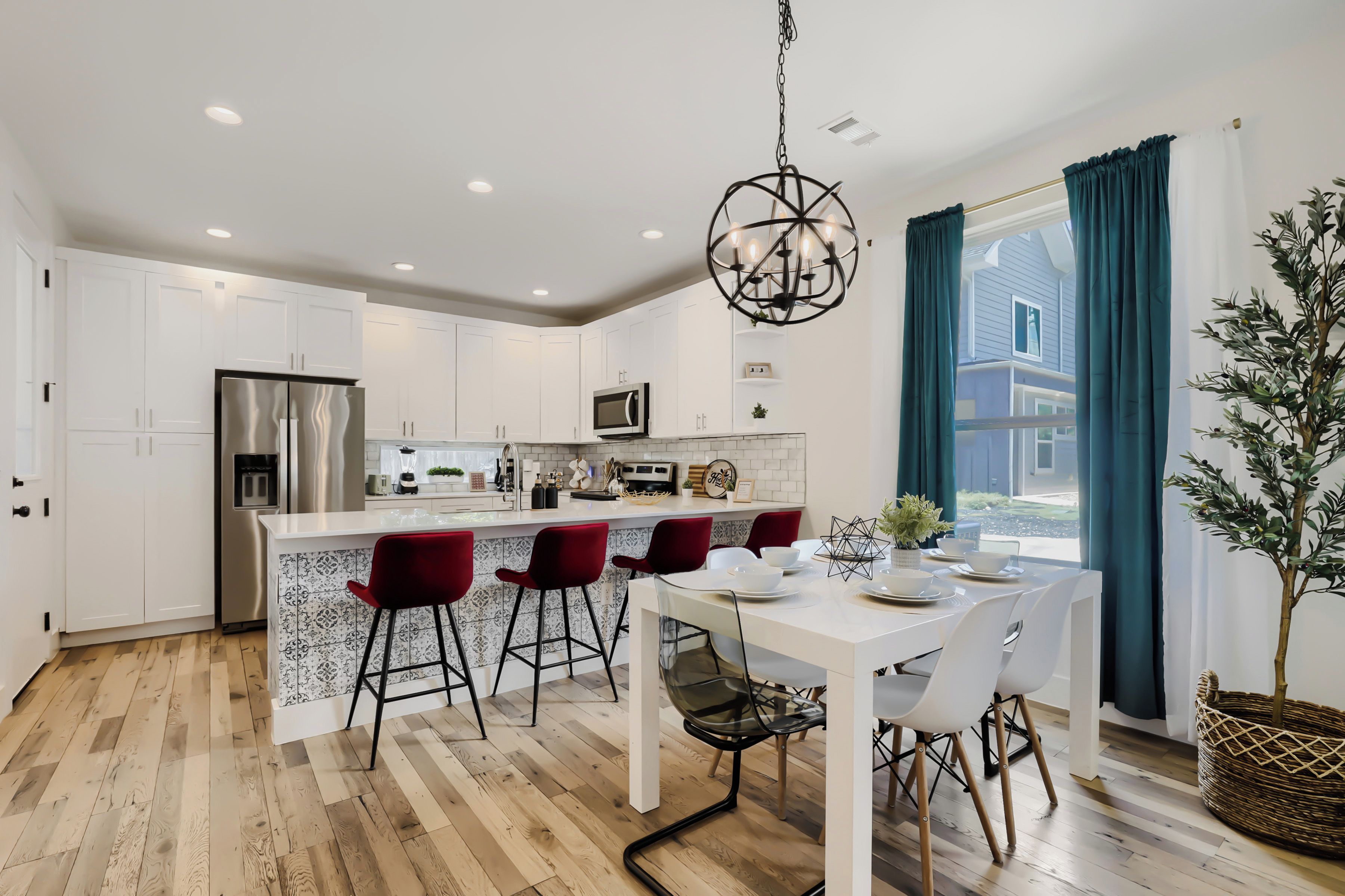 A modern kitchen with white cabinetry, a stainless steel refrigerator, a central island with bar stools, and a hanging light fixture.