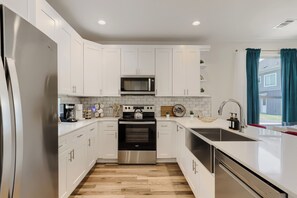 A modern kitchen with white cabinetry, stainless steel appliances, and a wooden floor. - Bold, Colorful Austin Retreat, Sleeps 9, Mins to Downtown, UT & Moody Center (Austin)