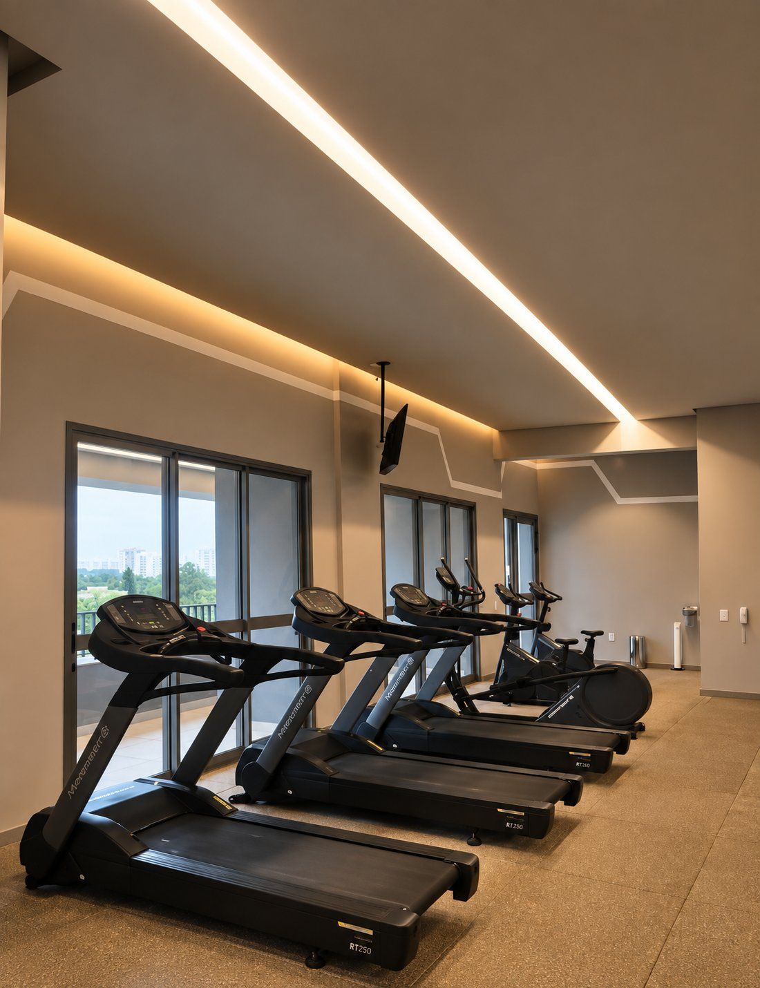 A gym with treadmills lined up against a wall with large windows.