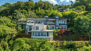 Ein modernes, zweistöckiges Haus mit Balkon, umgeben von üppiger Vegetation.